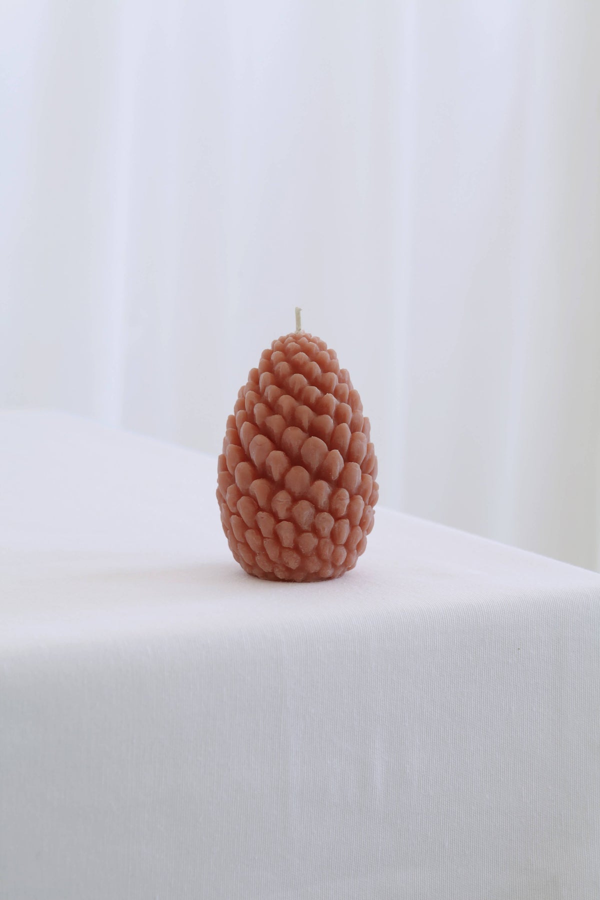 Pine cone-shaped candle on a white surface with a light background