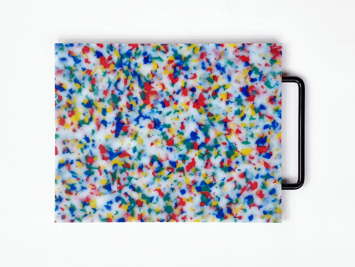 Multicolored speckled cutting board with a black handle on a white background
