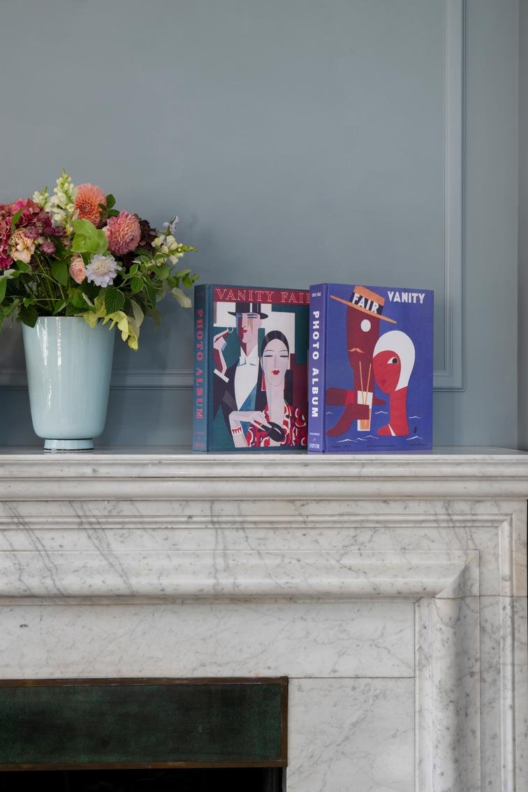 Two books on a fireplace mantle with a vase of flowers next to them.