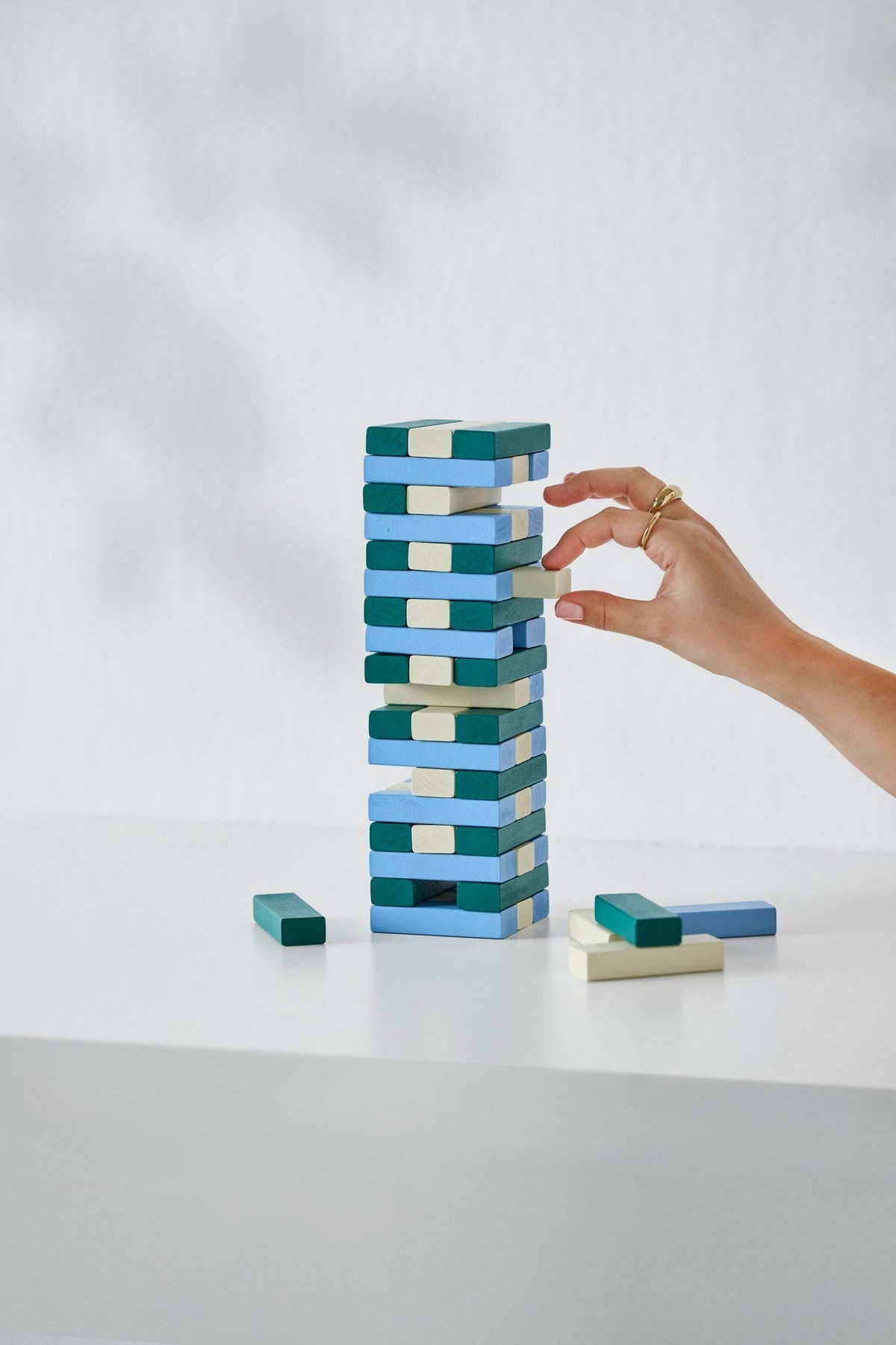 Hand placing a block on a tower of colorful wooden blocks against a white background